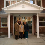 One of the founding families in front of the entrance to their new home at Serviam Gardens.